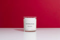Candle in a clear container with a white label on a red background