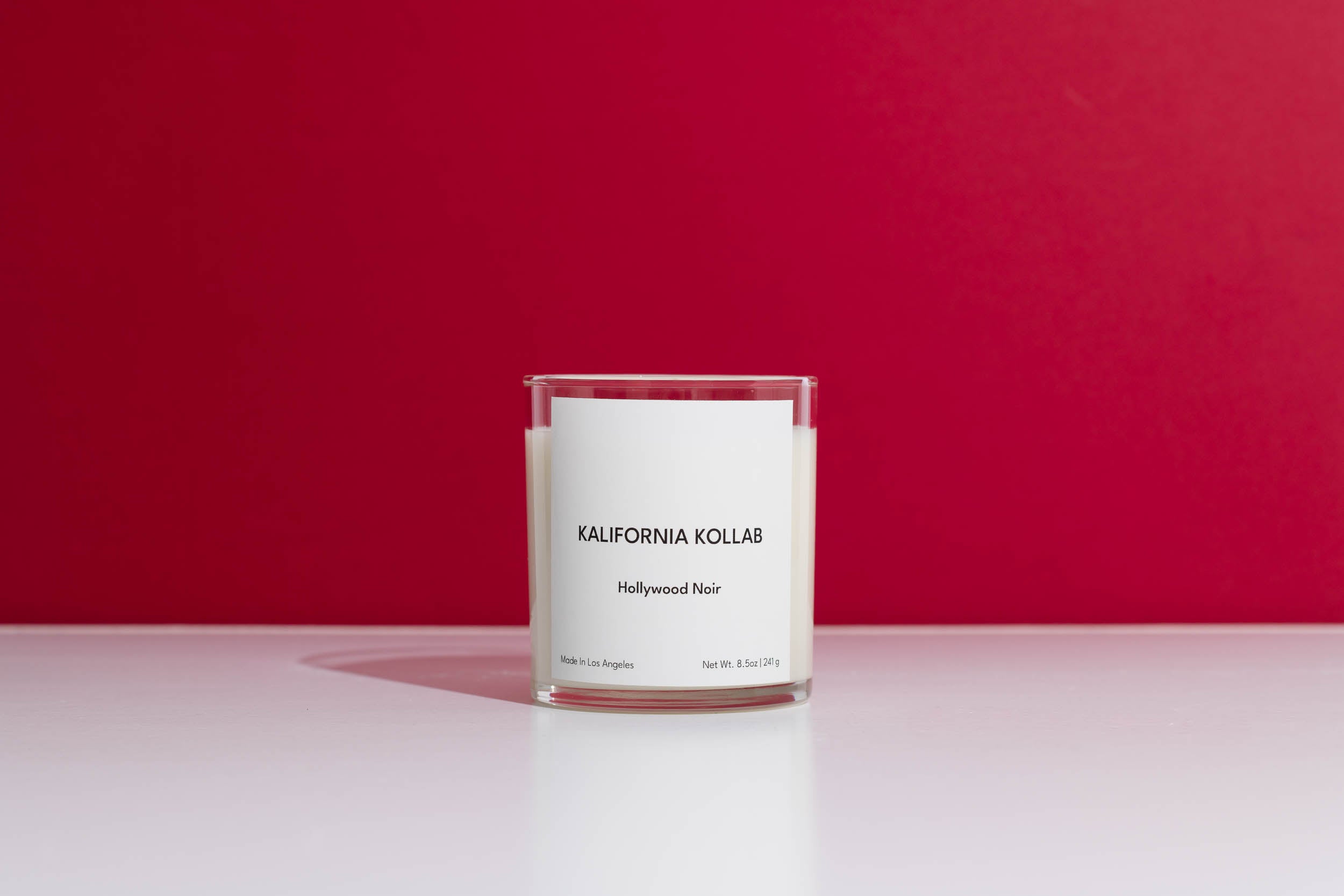 Candle in a clear container with a white label on a red background