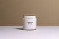 A clear glass jar candle with white wax and a white label reading 'CALIFORNIA COLLAR' and 'TOPANGA RITUAL', set on a white surface against a warm beige background.