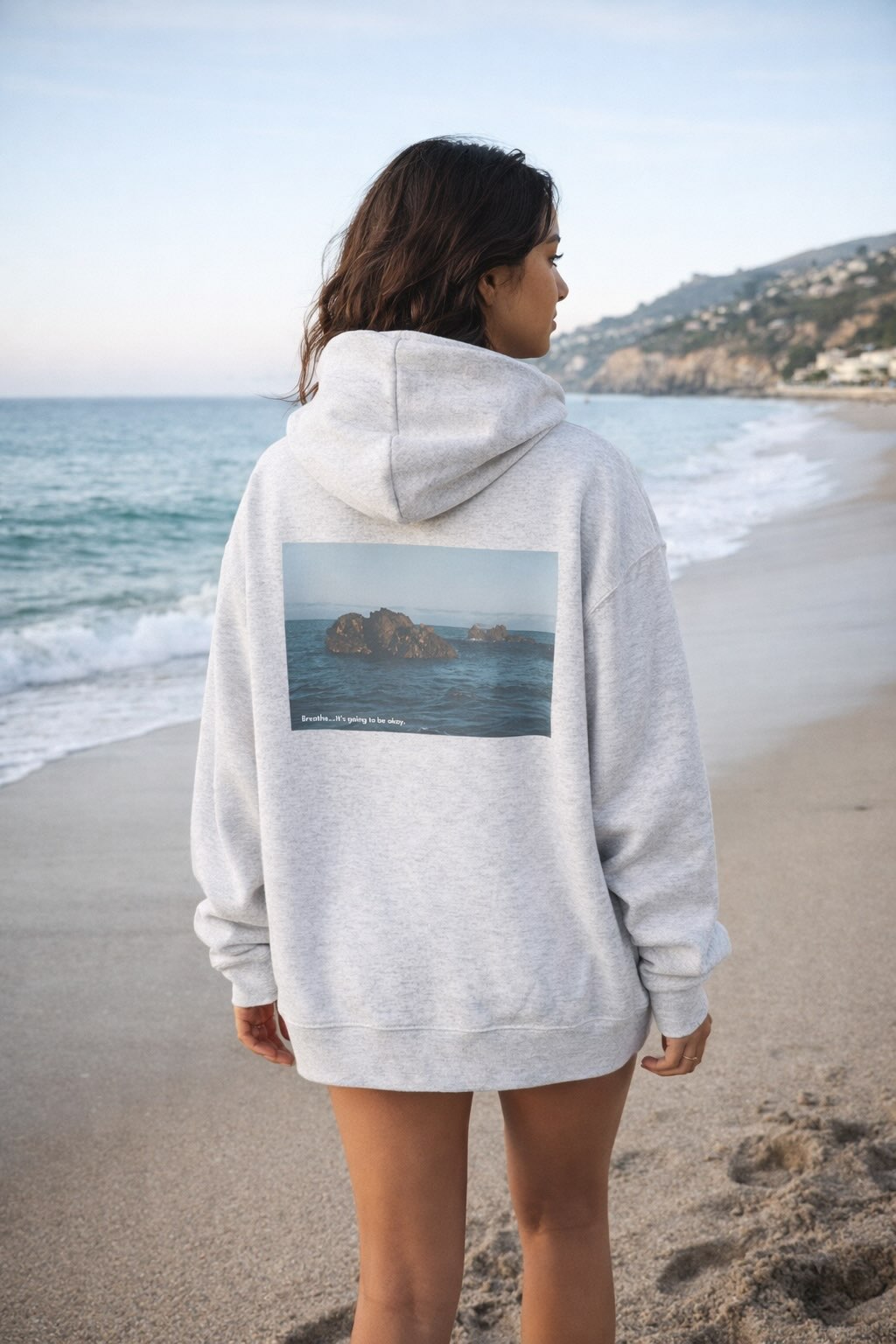Person wearing a hoodie with a scenic print on a beach